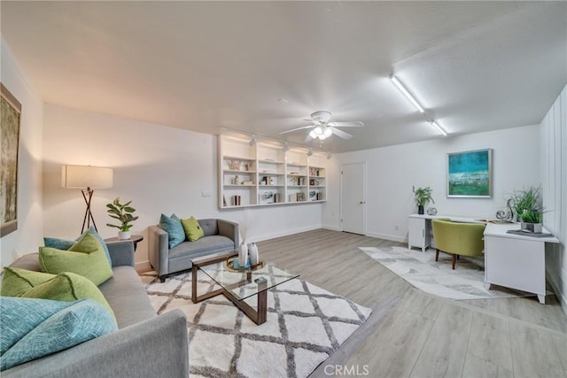 living room with ceiling fan, baseboards, and light wood-style floors