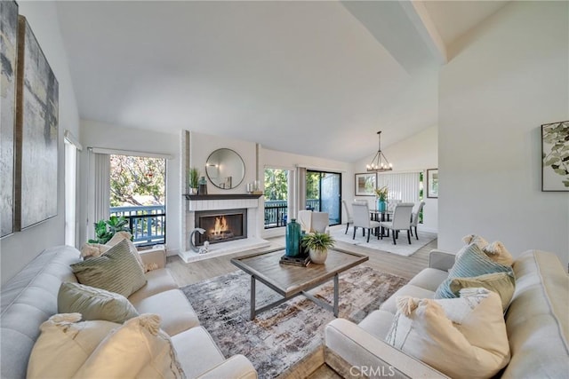 living room with a chandelier, a brick fireplace, high vaulted ceiling, and light wood-style flooring