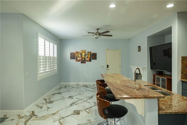 kitchen featuring baseboards, stone counters, marble finish floor, a ceiling fan, and a sink