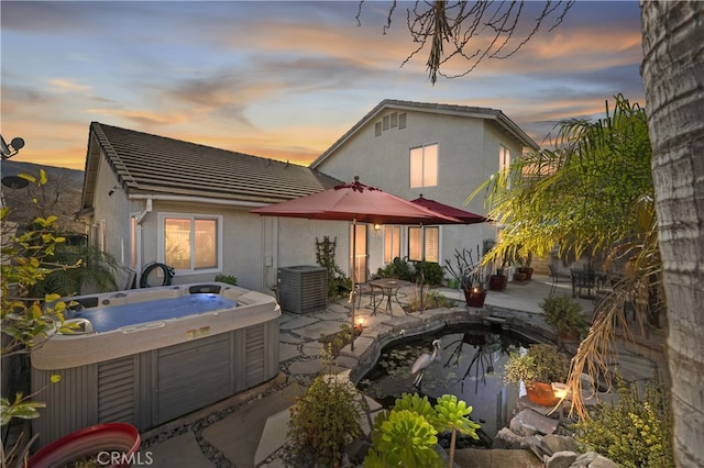 back of property featuring central AC, a patio area, a hot tub, and stucco siding