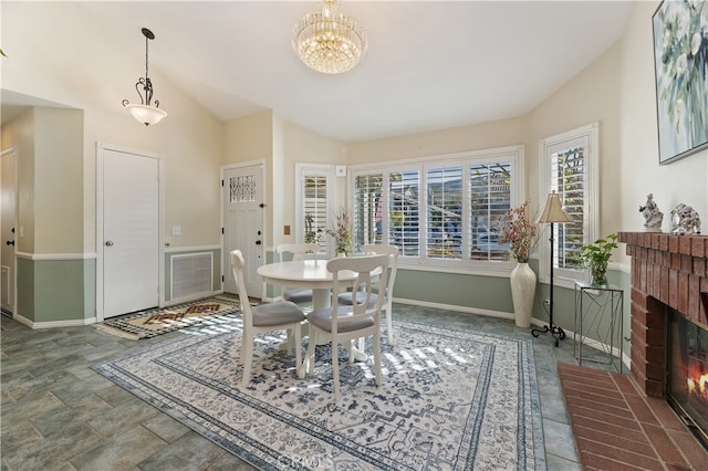 dining room with baseboards, visible vents, lofted ceiling, an inviting chandelier, and a brick fireplace