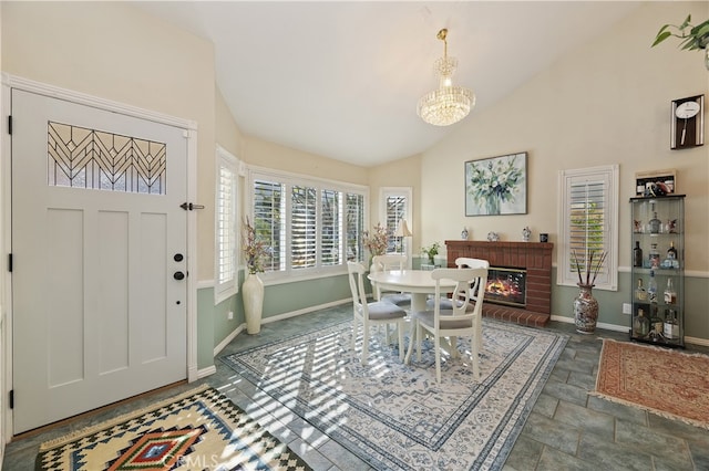 dining room featuring baseboards, stone finish flooring, a brick fireplace, high vaulted ceiling, and a notable chandelier