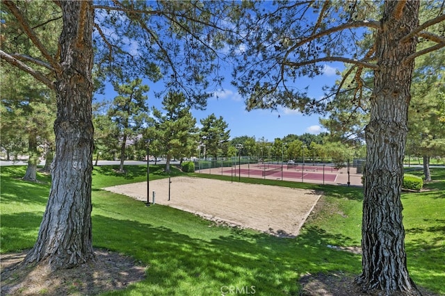 view of property's community with a tennis court, a lawn, volleyball court, and fence