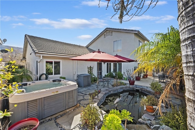 rear view of property with stucco siding, a patio area, a hot tub, and central air condition unit