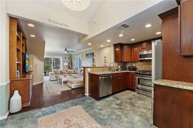 kitchen featuring light stone counters, stainless steel appliances, visible vents, open floor plan, and a peninsula