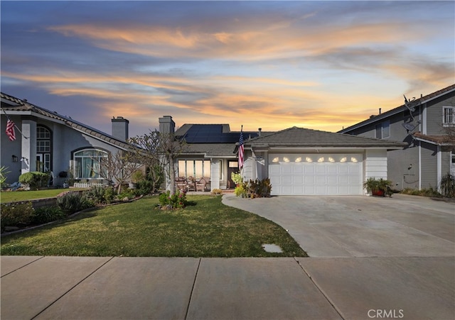 view of front of house with driveway, a lawn, an attached garage, and roof mounted solar panels