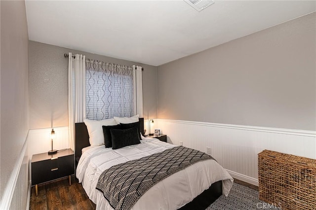 bedroom with wainscoting, wood finished floors, and visible vents