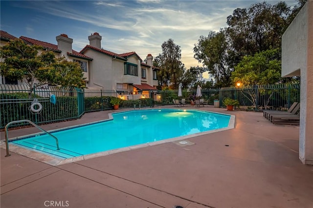 pool at dusk with a patio area, a community pool, and fence