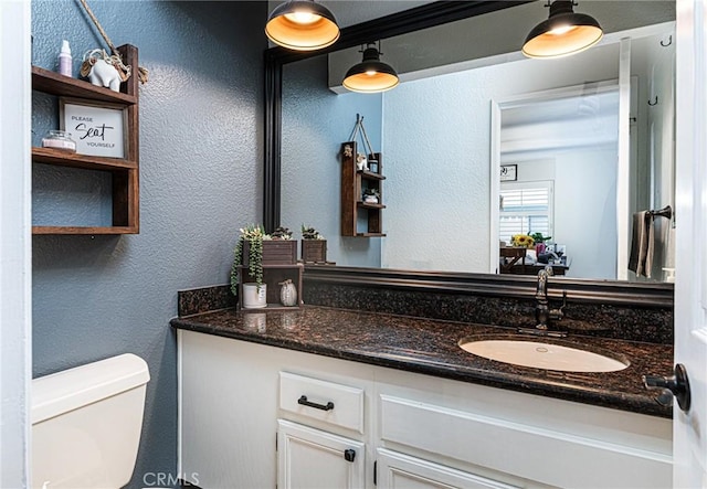 bathroom featuring toilet, a textured wall, and vanity