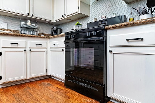 kitchen featuring light wood-type flooring, white cabinets, black range with gas cooktop, and dark stone countertops