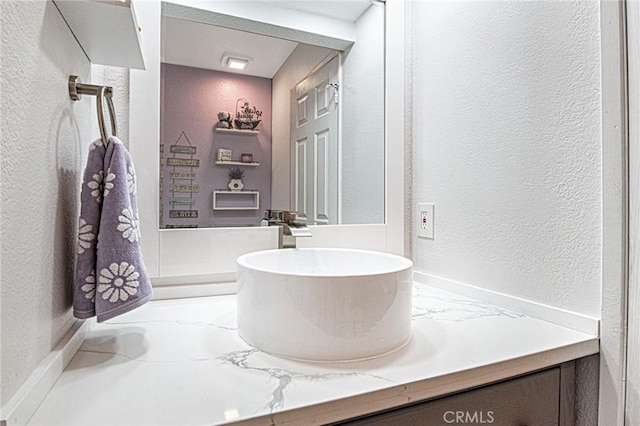 bathroom featuring marble finish floor, a textured wall, and vanity