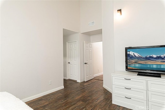 unfurnished bedroom featuring dark wood-style floors, baseboards, a high ceiling, and visible vents