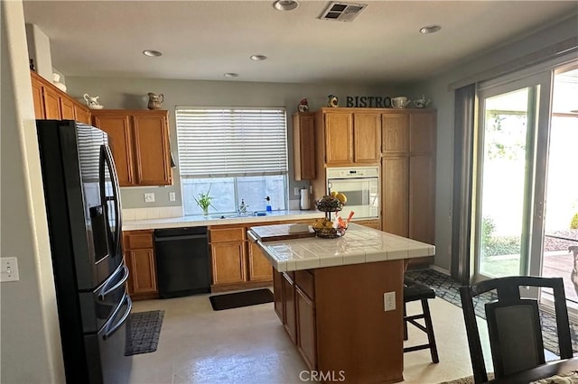 kitchen with visible vents, brown cabinets, black appliances, a center island, and tile countertops