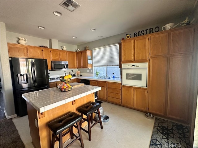 kitchen featuring visible vents, black appliances, a kitchen island, brown cabinetry, and tile counters