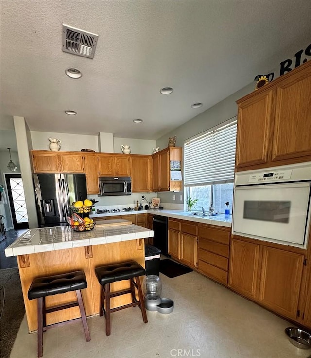 kitchen featuring visible vents, tile countertops, dishwasher, white oven, and stainless steel fridge