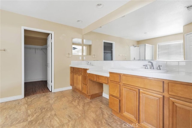 bathroom with a walk in closet, a sink, baseboards, and double vanity