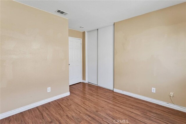 empty room with wood finished floors, visible vents, and baseboards