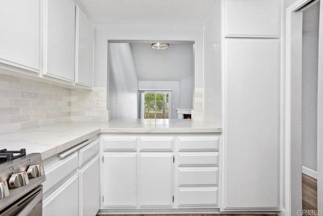 kitchen featuring gas range, light stone counters, white cabinets, and backsplash