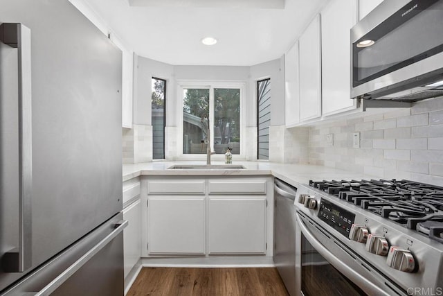 kitchen with dark wood-type flooring, a sink, white cabinetry, light countertops, and appliances with stainless steel finishes