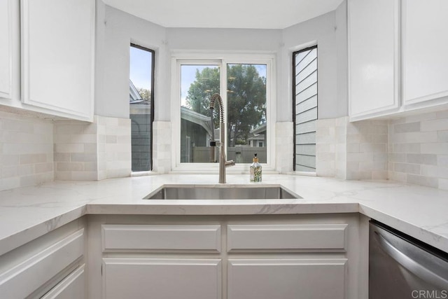 kitchen featuring stainless steel dishwasher, a sink, light stone counters, and white cabinets