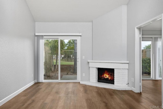 unfurnished living room with a brick fireplace, wood finished floors, and a healthy amount of sunlight