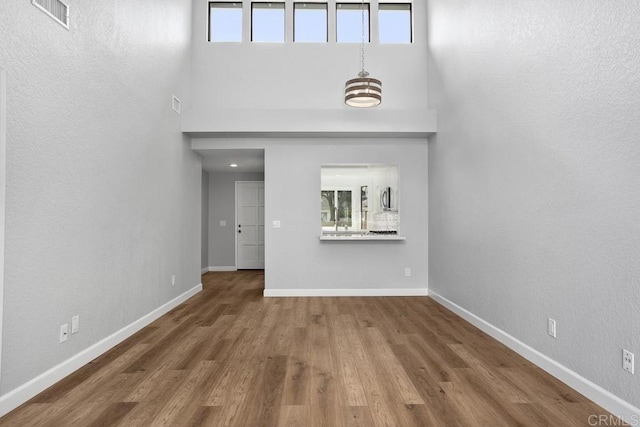 unfurnished living room featuring visible vents, a towering ceiling, baseboards, and wood finished floors