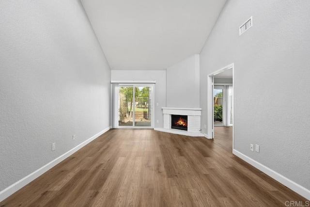 unfurnished living room featuring a textured wall, a fireplace, wood finished floors, visible vents, and baseboards