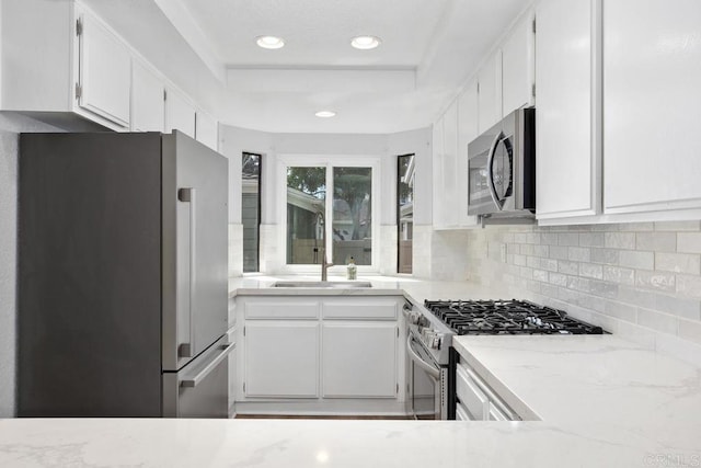 kitchen featuring backsplash, light stone countertops, stainless steel appliances, white cabinetry, and a sink