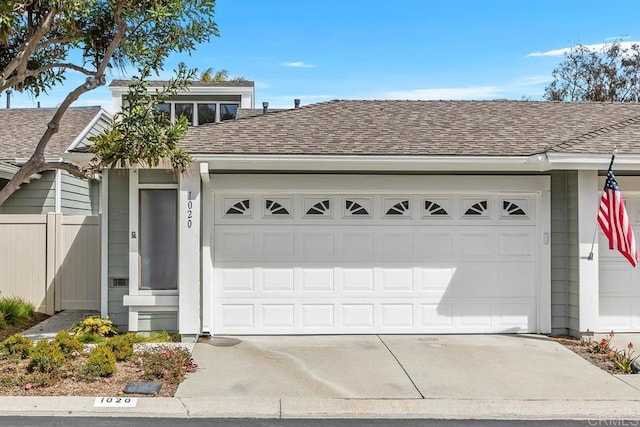 view of front of property with a shingled roof, concrete driveway, and fence