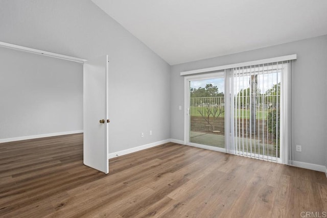 spare room with baseboards, vaulted ceiling, and wood finished floors