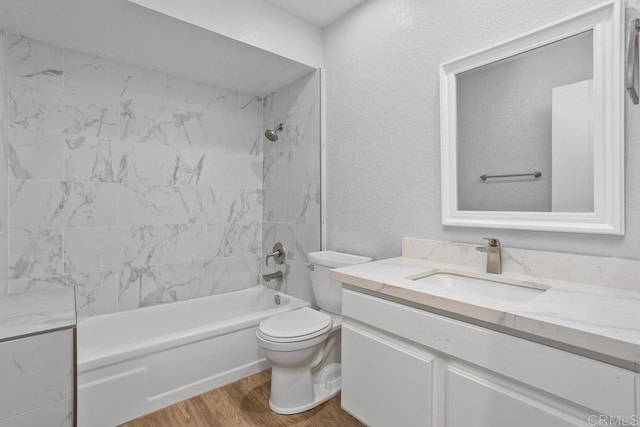 full bath featuring a textured wall, toilet, tub / shower combination, vanity, and wood finished floors