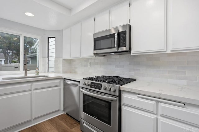 kitchen with stainless steel appliances, white cabinets, light stone countertops, dark wood-style floors, and tasteful backsplash