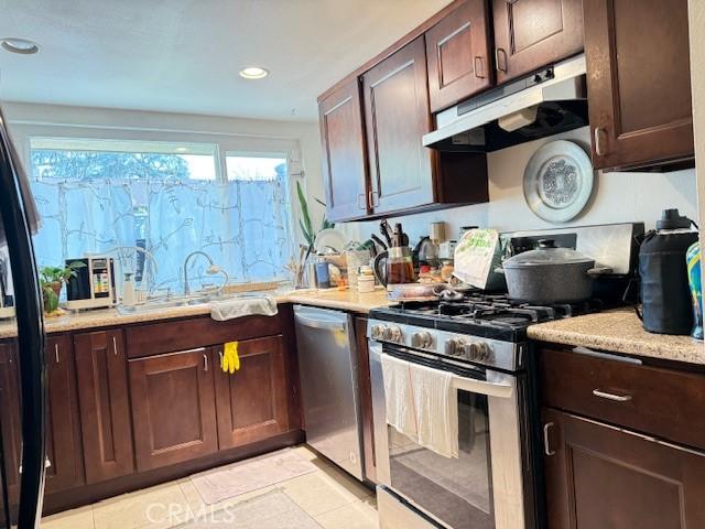 kitchen featuring dark brown cabinets, under cabinet range hood, light countertops, stainless steel appliances, and a sink