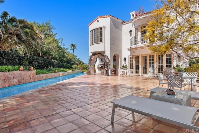 back of property with a patio, a balcony, a fenced in pool, stucco siding, and a tiled roof