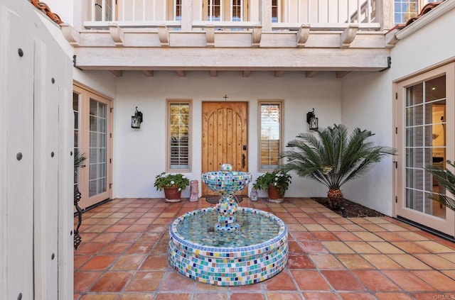 view of exterior entry featuring stucco siding, a balcony, french doors, and a patio area