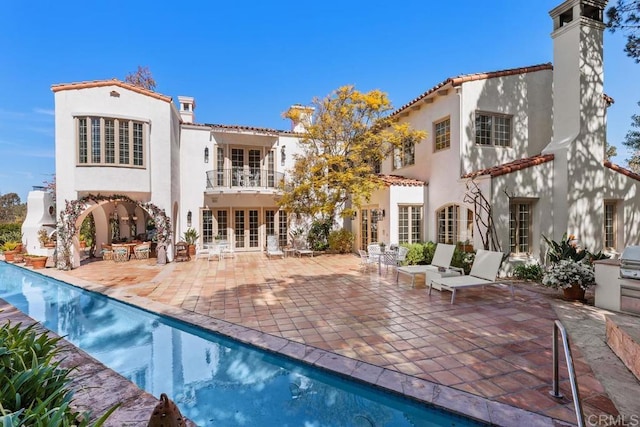 rear view of house featuring a patio area, a balcony, french doors, and stucco siding