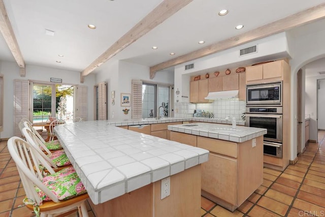 kitchen featuring backsplash, a center island, tile counters, light brown cabinetry, and stainless steel appliances