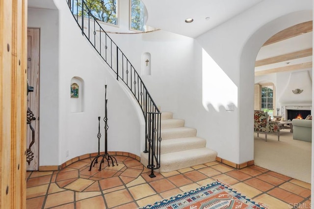 foyer with baseboards, stairway, light tile patterned floors, a warm lit fireplace, and arched walkways