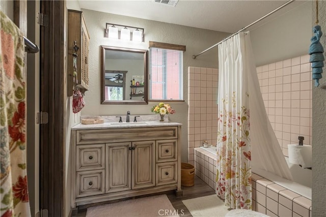 bathroom with visible vents, a textured wall, tiled shower / bath combo, vanity, and wood finished floors