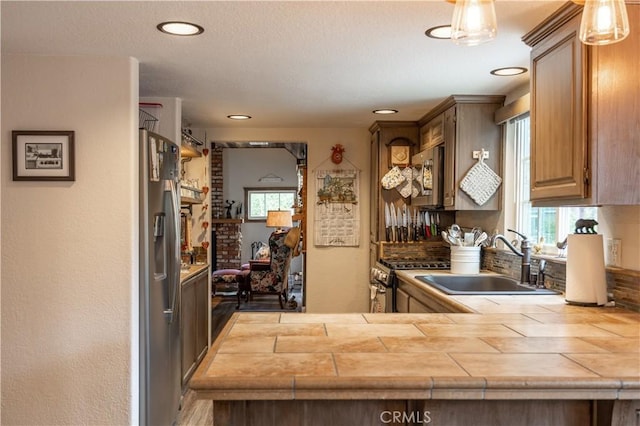 kitchen with a peninsula, appliances with stainless steel finishes, a sink, and tile counters