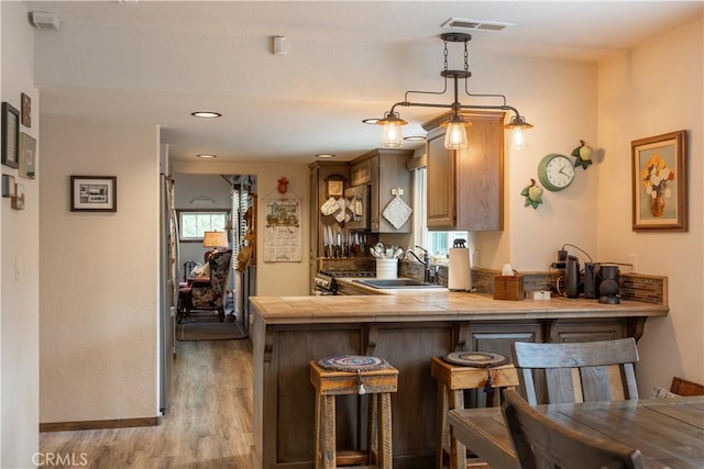 kitchen with a breakfast bar, tile countertops, light wood-style floors, a sink, and a peninsula