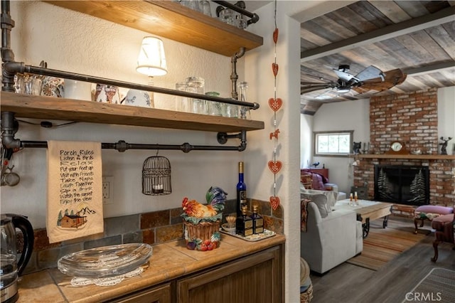 interior space with a fireplace, a ceiling fan, tile counters, open shelves, and beamed ceiling