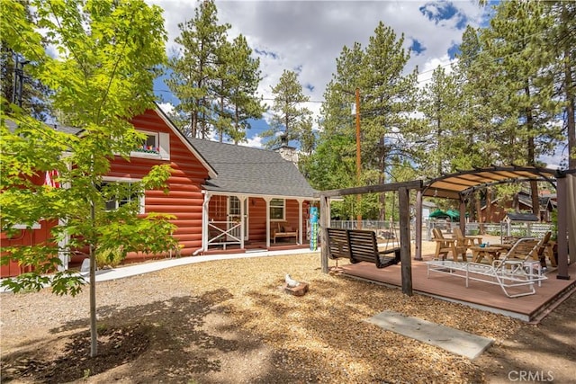 back of house with a wooden deck, fence, a pergola, and roof with shingles