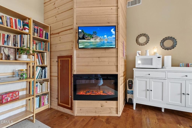 sitting room featuring dark wood-style floors, visible vents, a glass covered fireplace, and wood walls