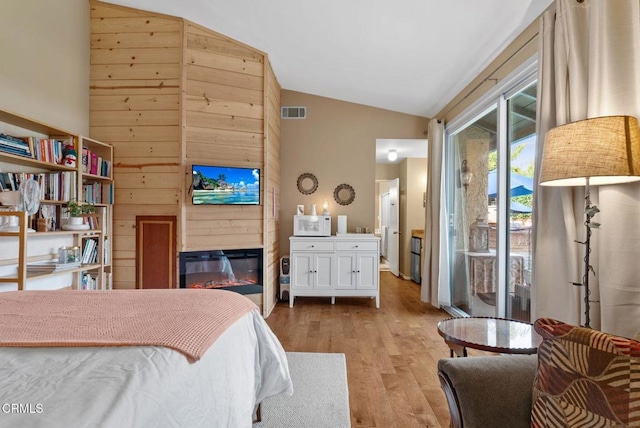 bedroom with wood finished floors, visible vents, access to exterior, vaulted ceiling, and a glass covered fireplace