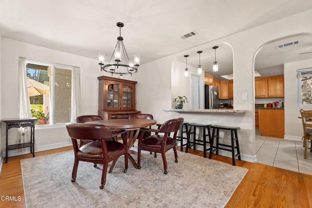 dining room featuring baseboards, light wood-style floors, visible vents, and a notable chandelier