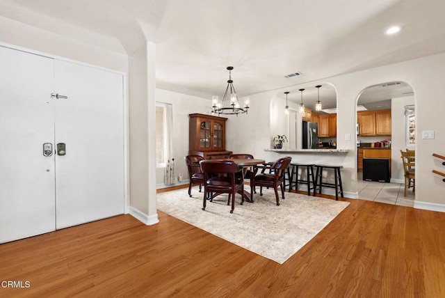 dining space featuring light wood finished floors, baseboards, visible vents, arched walkways, and a chandelier