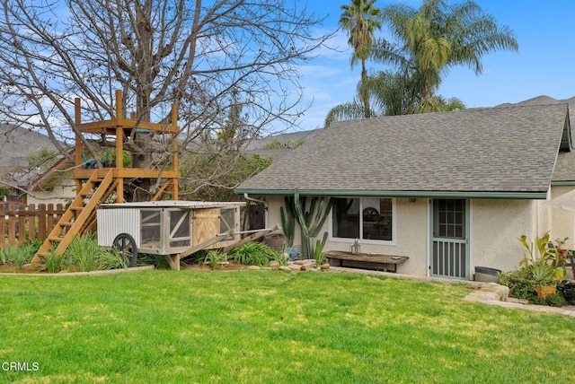 exterior space with roof with shingles, fence, a lawn, and stucco siding