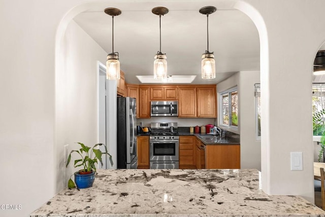 kitchen featuring arched walkways, light stone counters, appliances with stainless steel finishes, decorative light fixtures, and a sink