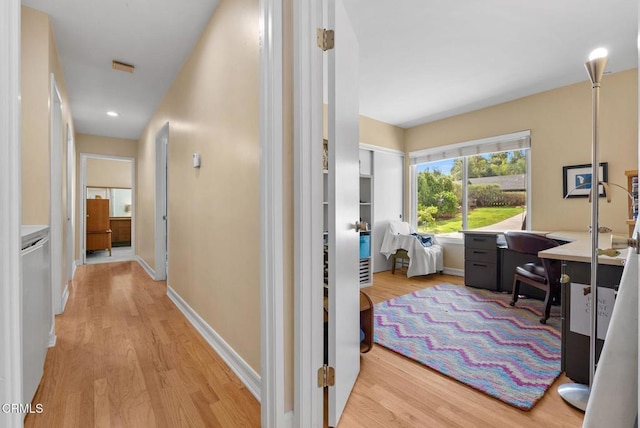 hall featuring baseboards, visible vents, and light wood finished floors